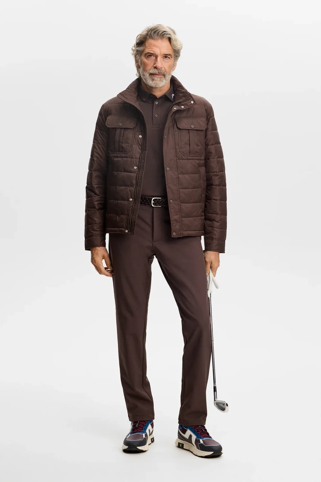 Golfer in a brown padded jacket and matching brown trousers holding a club